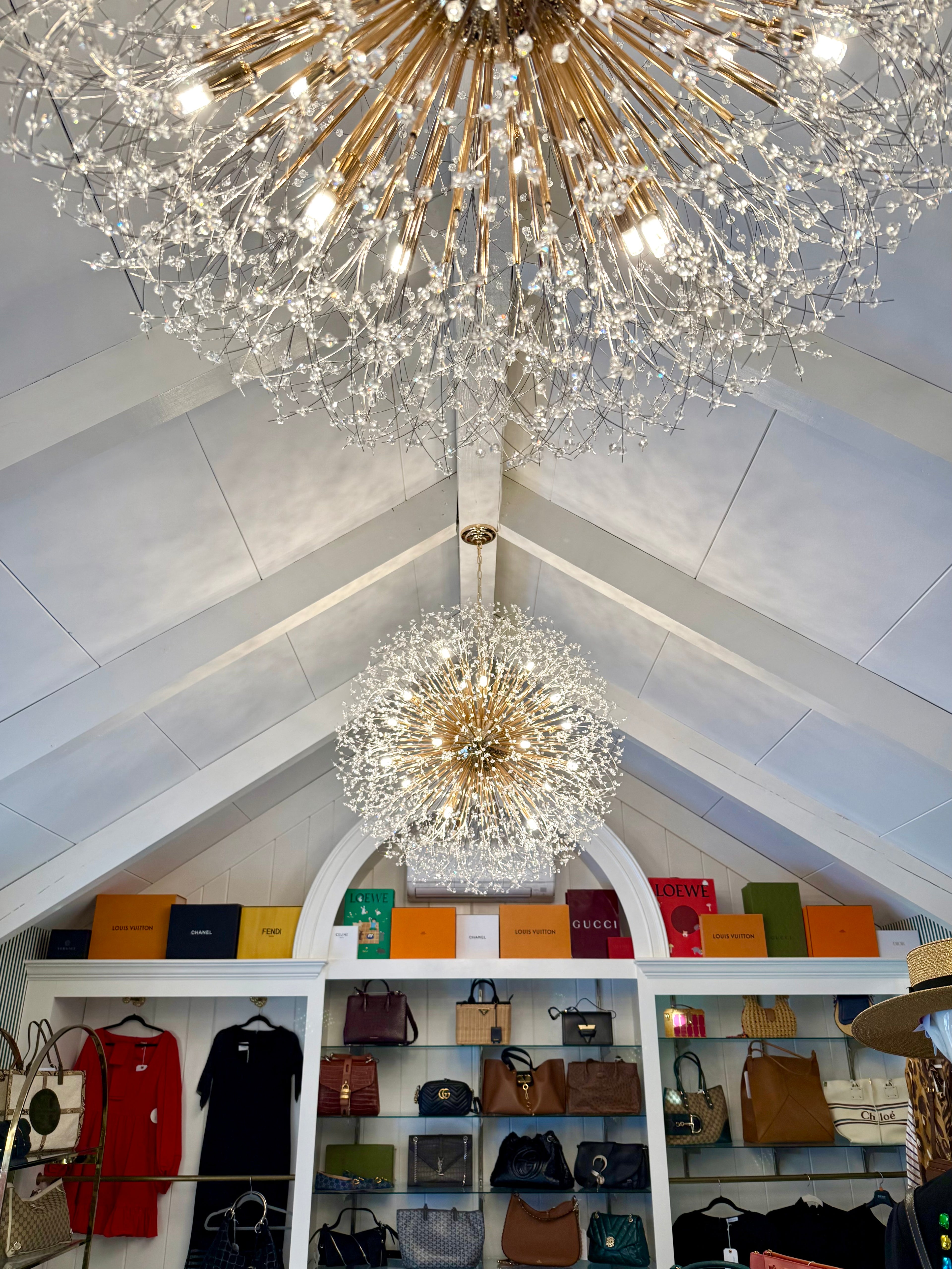 Luxurious chandeliers hanging from a vaulted ceiling with a display of handbags and clothing below.