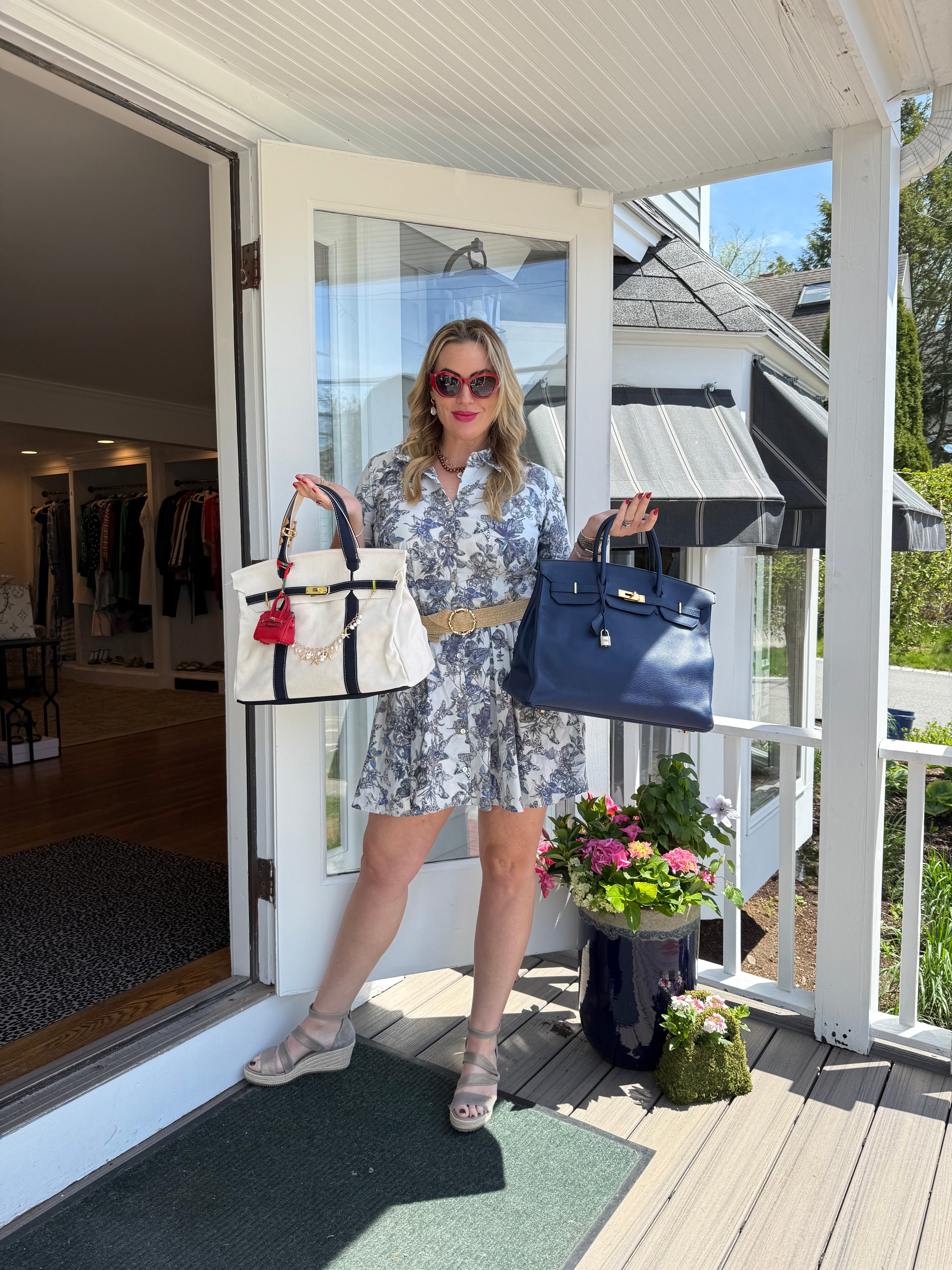 Woman standing on a porch of a boutique with two handbags, a white and blue Boatkin and a navy Hermès Birkin.