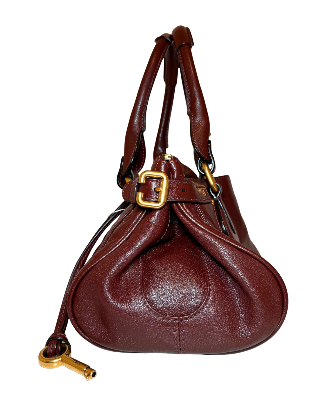 A dark reddish-brown leather handbag with gold-tone hardware, featuring dual top handles, and a decorative gold buckle on a white background.